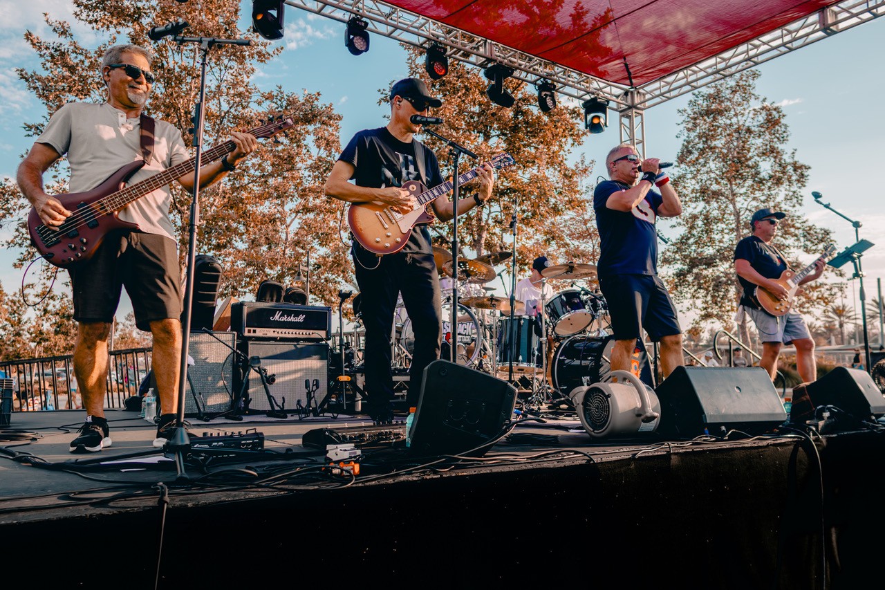 Band members of Diego's Garage standing on stage and playing music on a sunny day.